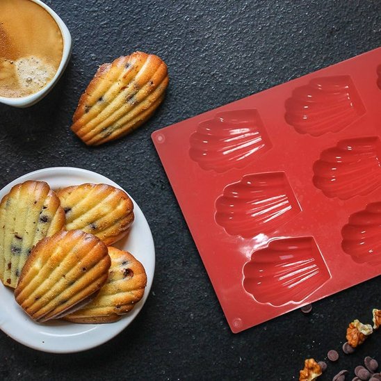 des madeleines aux pépites de chocolat sur une assiette, avec une tasse de café et un moule en silicone rouge à côté