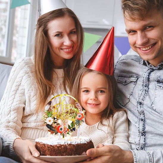 famille souriante avec des chapeaux de fête, tenant un gâteau d'anniversaire décoré d'un deco gateau floral "Happy Birthday"
