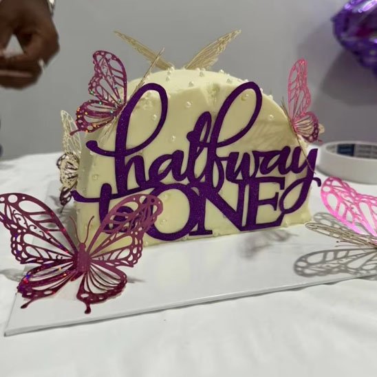 gâteau décoré avec un deco gateau topper "halfway done" et des papillons en métal rose et violet sur fond blanc.