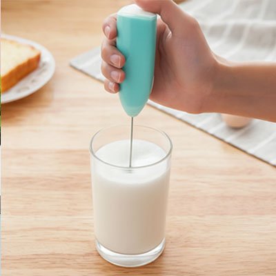 main utilisant un mousseur a lait pour faire mousser du lait dans un verre avec une tranche de pain en arrière-plan