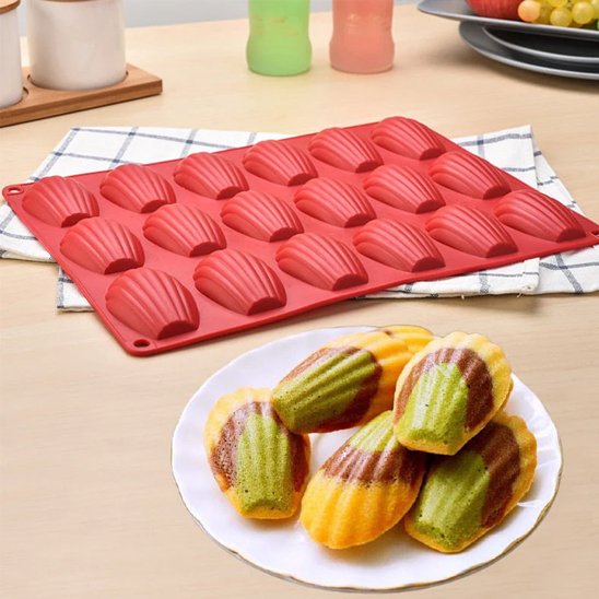 moule en silicone rouge avec des empreintes de madeleines, accompagné d'une assiette de madeleines colorées vertes et jaunes