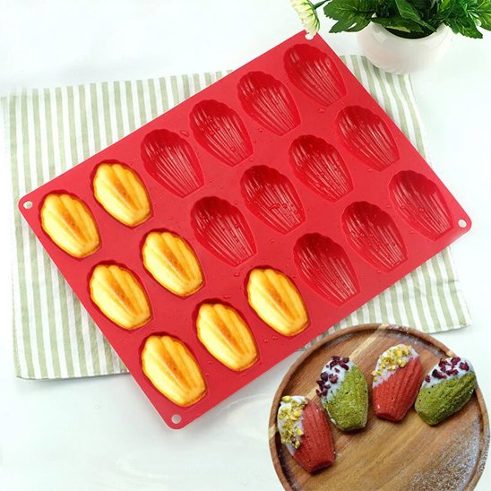 moule en silicone rouge avec des madeleines dorées à moitié cuites accompagnées d'une assiette de madeleines décorées de garnitures colorées