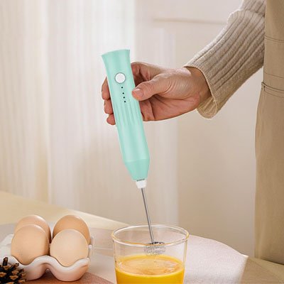 Mousseur à lait vert fouettant des œufs dans un verre