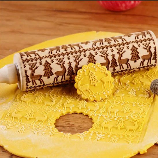 rouleau à pâtisserie en bois décoré de rennes et sapins, utilisé pour imprimer des motifs sur de la pâte jaune