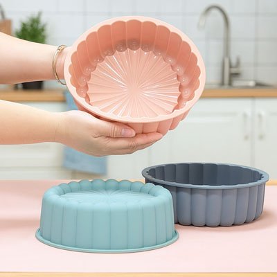 un moule en silicone rose tenu par quelqu'un avec d'autres moules en silicone bleu et gris posés sur une surface de cuisine