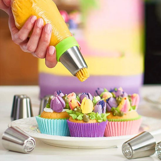 Une personne décore des cupcakes colorés avec une poche à douille remplie de crème jaune