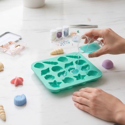 Une personne verse un liquide coloré dans un moule en silicone en forme de coquillages