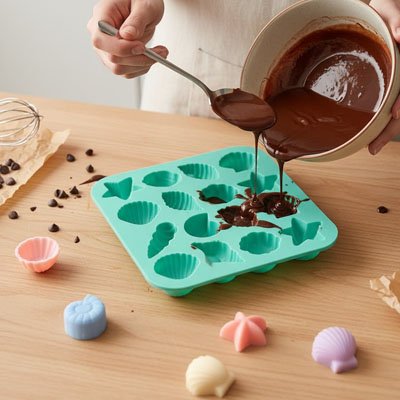 versant du chocolat fondu dans un moule en silicone vert en forme de coquillages et d’étoiles de mer